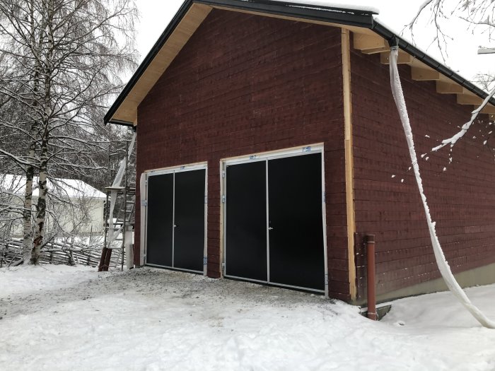 Två monterade industriella garageportar på en tegelbyggnad, med snötäckt mark och is istappar på taket.