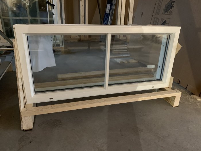 Ett nytt fönster på träpall i ett byggprojektområde, redo för installation i ett garage.