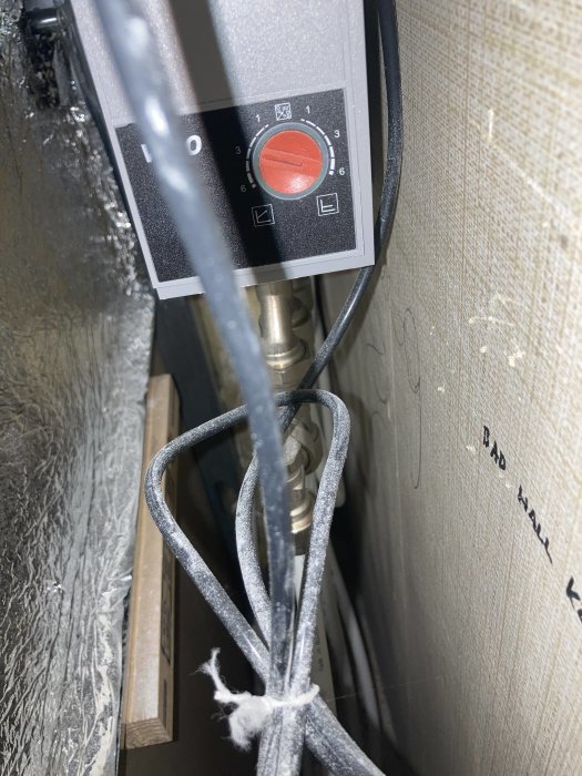 Bild på installationer genom inspektionslucka, visar rör, kablar och en apparat med vred.