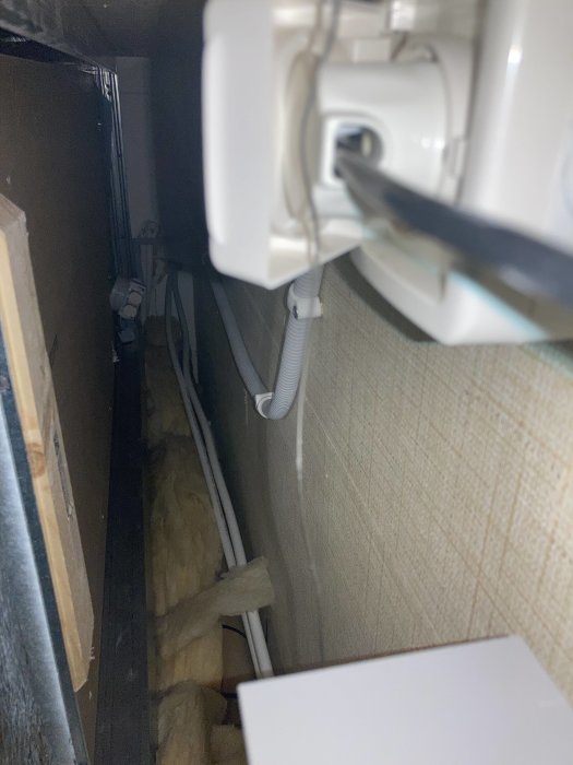 Vy genom inspektionslucka med synliga rör och isolering mellan kök och badrum.