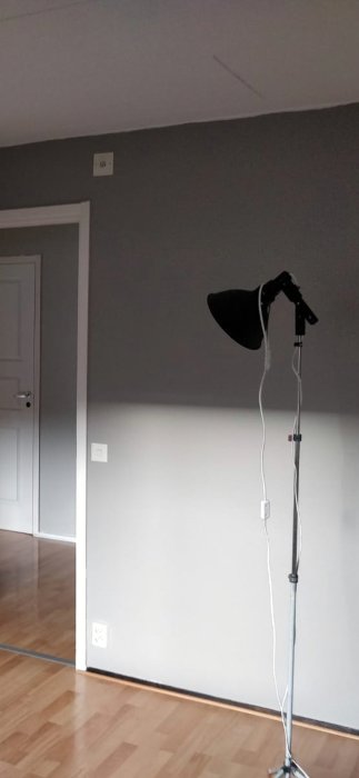 Hörn av ett rum med parkettgolv och olika färgade golvlist och kvartstav vid dörren och väggen.
