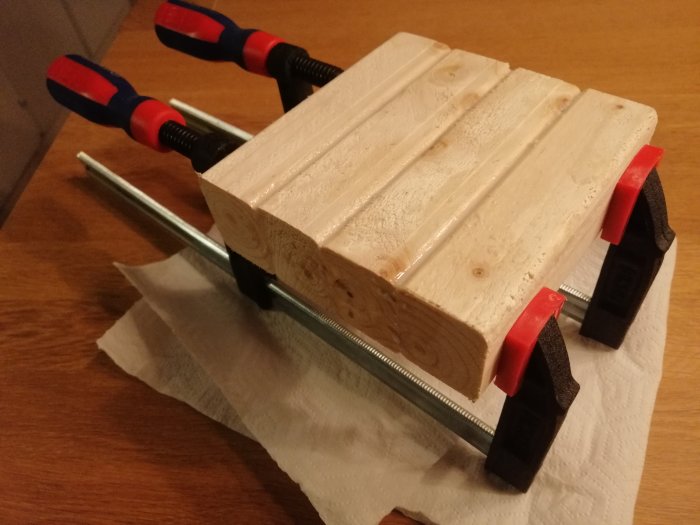 Trästycke fastklämt i skruvstäd på bänk under tillverkning, verktyg och material syns.