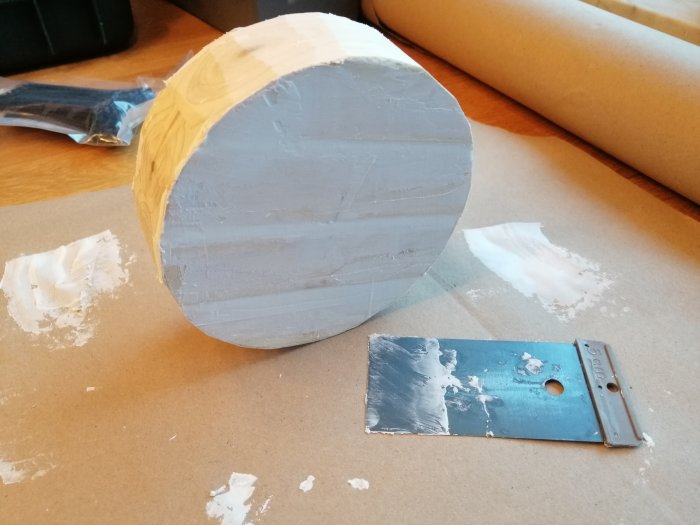 Rund träbit belagd med spackel bredvid en spackelspade på arbetsbord, pysselprojekt i arbete.
