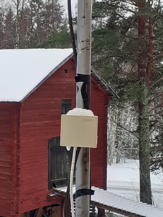 En dosa med svart och vit antennsladd på balkongen med snö och röd stuga i bakgrunden.