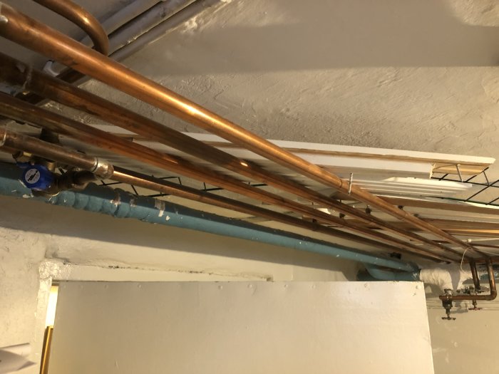 Värmesystemets rörledningar i källartak med en luftventil och synliga kopplingar.