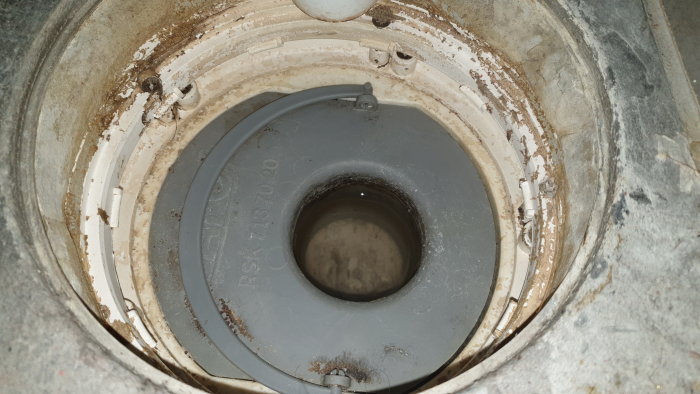 Plastinsats i golvbrunn med synligt vattenlås och omslutande smutsiga kanter.