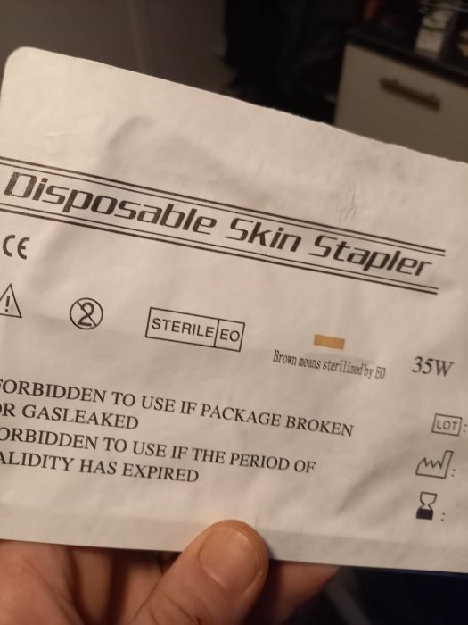 Hand håller förpackning för engångsbruk av hudklammer, märkt "Disposable Skin Stapler".