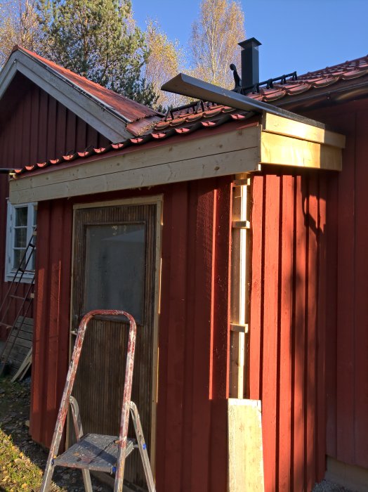 Byggprojekt med nytt tak under konstruktion på röd byggnad med stege och byggmaterial.