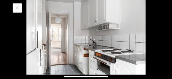 Kök med vit inredning och spis, vit kakelvägg, från en renoveringsklar bostadsrätt med 60-tals charm.