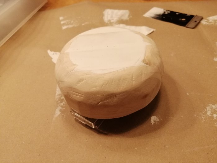 Rund träskulptur under bearbetning för att likna en nyckelpigas kropp, med slipverktyg i bakgrunden.
