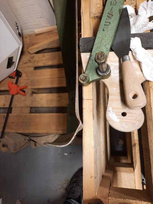 Verkstadsbild med suva, trädetaljer och verktyg för reparation, inklusive ett böjt skydd och rätad planka.