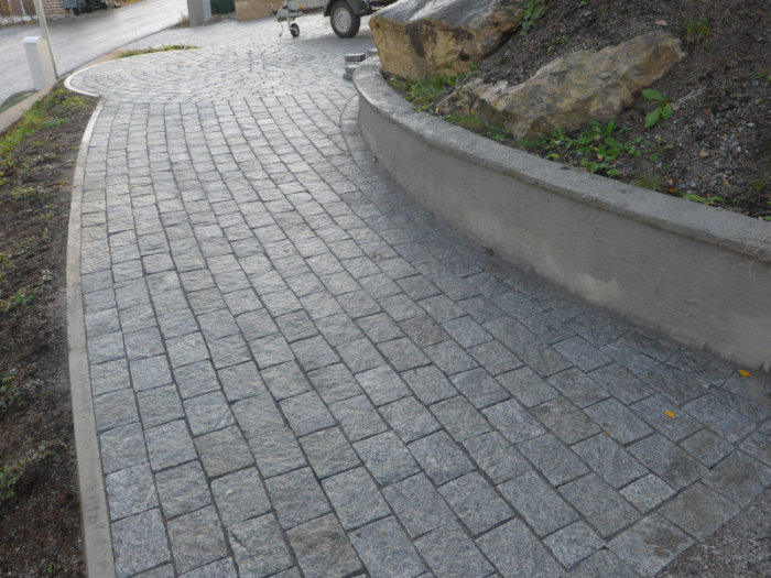 Ny lagd grå storgatsten i ett böjt mönster längs en kurvig trottoarkant.