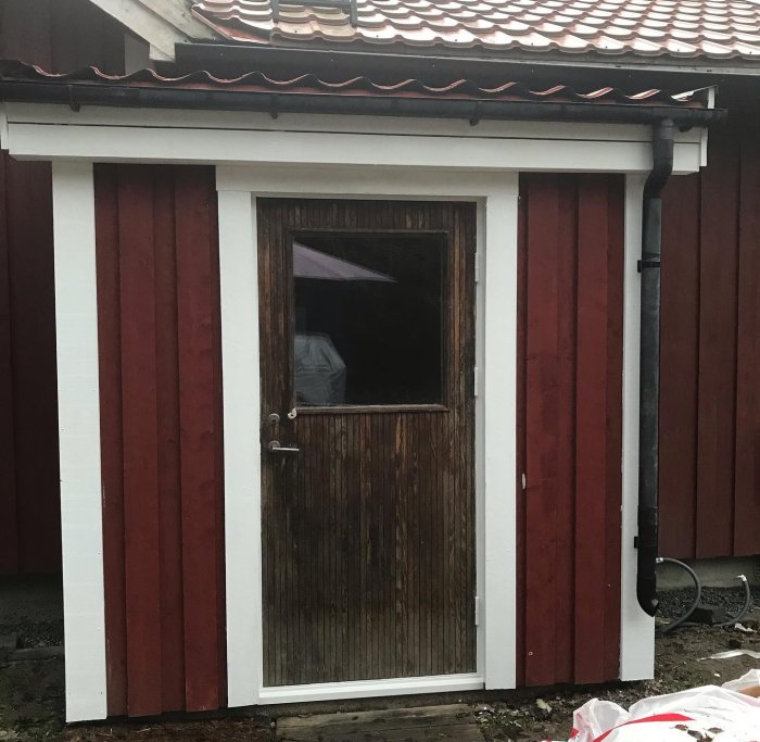 En nybyggd bod med råspontklädd fasad och ett målat betonggolv, delvis öppen dörr visar insidan.