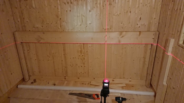 Byggplats för lav i bastu med en laserlinje som markerar nivån för montering av lavram, regel och isolering synliga.