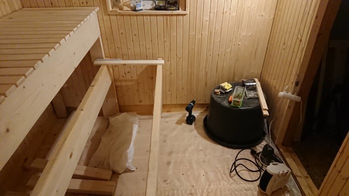 Konstruktion av bastulavar med synliga träreglar och verktyg i en bastu under renovering.