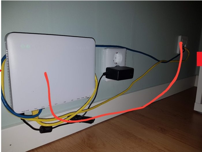 Router med rörigt kabelarrangemang monterad vid vägg ovanför golvlisten.