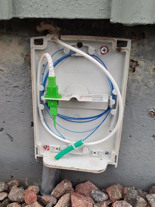 Öppen anslutningsbox på husvägg med fiberkabel och optisk utrustning, redo för patchning.