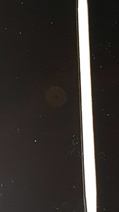 Närbild på glashäll med en synlig defekt och en tandpetare vid sidan, med reflexion och dammkorn.synlig defekt och en tandpetare vid sidan, med reflexion och dammkorn.