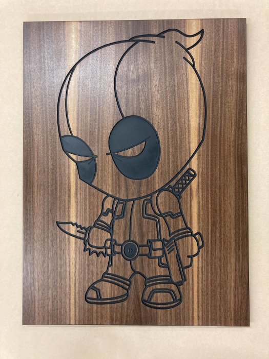 Inristad figur i valchromat och valnötsfaner, behandlad med hårdvaxolja, mot träbakgrund.