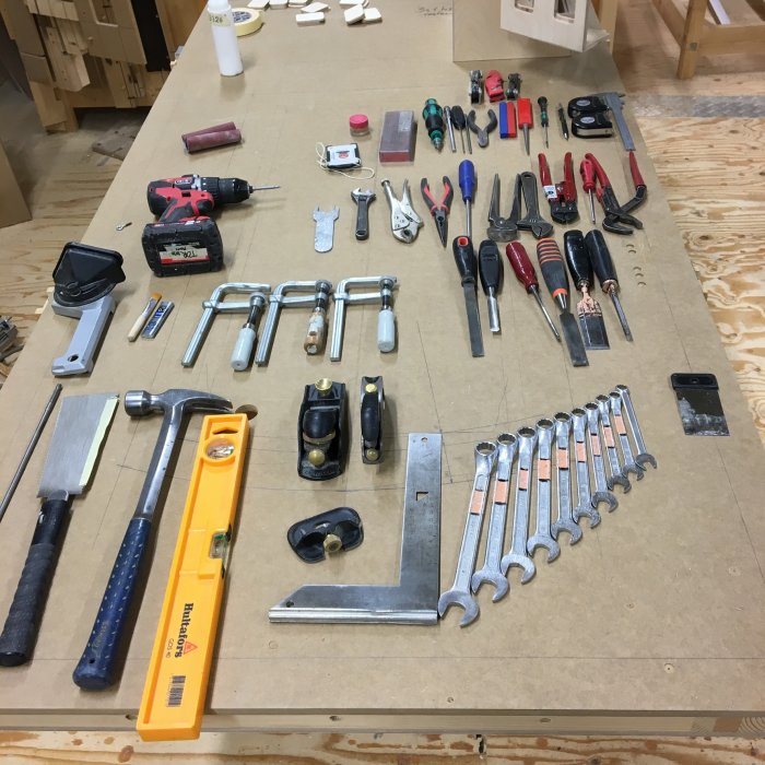 Verktyg ordnade på arbetsbänk: hammare, borrmaskin, nycklar, såg och måttverktyg.