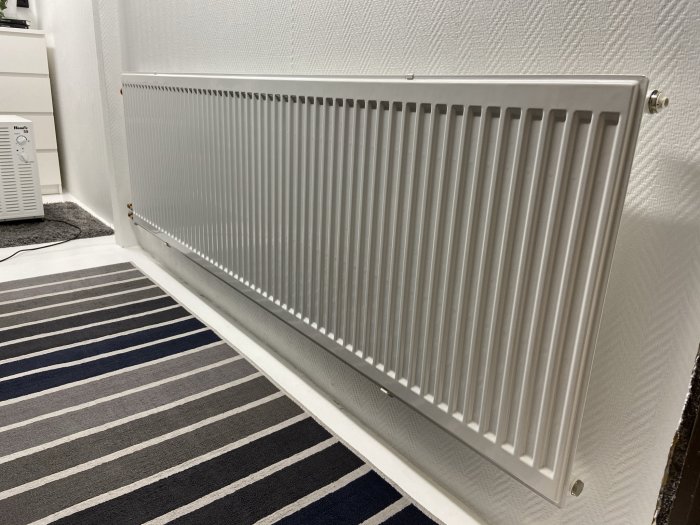 Väggmonterat radiatorvärmeelement på 200 cm i ett rum med randig matta.