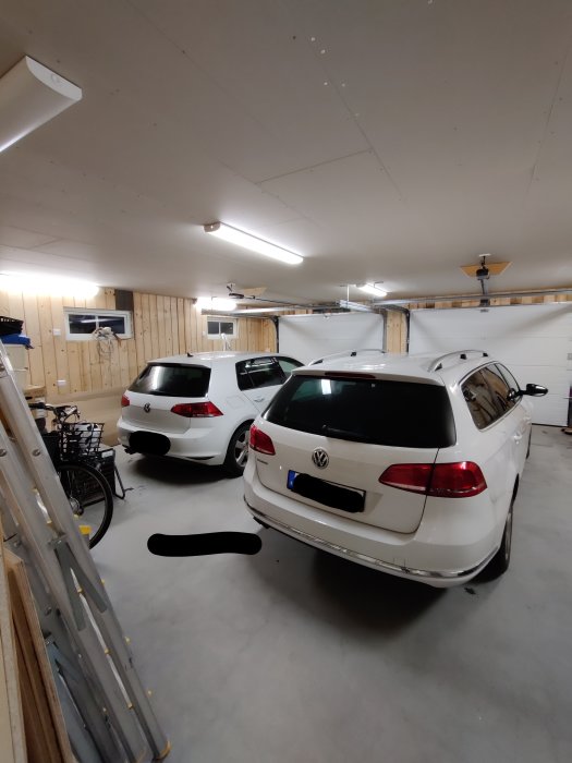 Renoverat garage med två vita bilar parkerade, panelväggar, och LED-belysning i taket.