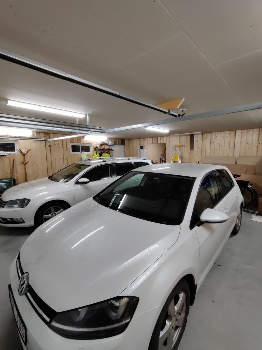 Ett nyrenoverat garage med två vita bilar och panelade väggar, och takbelysning.