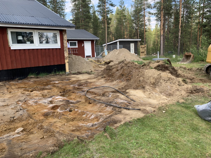 Grävningsarbete vid bostad med synliga vattenledningar och högar av grävd jord.