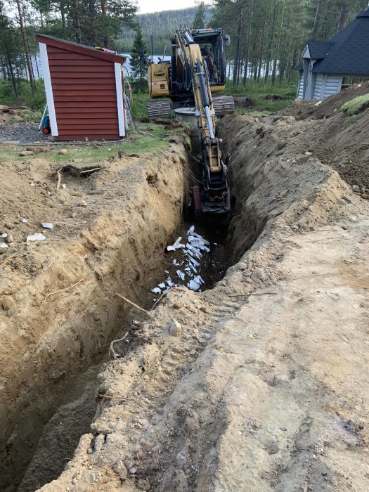 Grävmaskin gräver en djup grävtrench för nya vattenledningar vid ett byggprojekt.