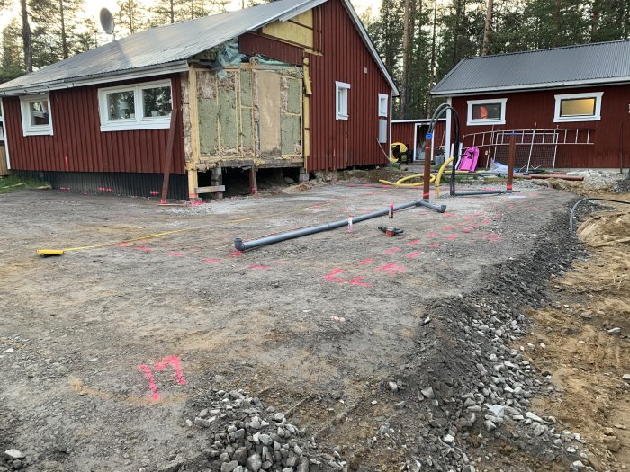 Renoveringsarbete vid hus med rivet hörn, avstängt område och märkning för vattenledningar på marken.