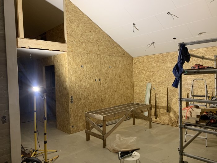 Pågående renovering med OSB-panel på vägg, omonterat golvsystem och byggmaterial.