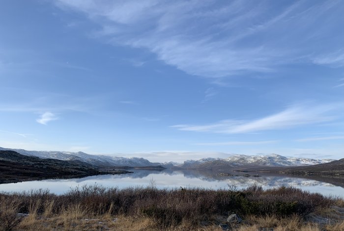 Spegelblank sjö med fjäll i bakgrunden under klar himmel i Hemsedal, Norge.