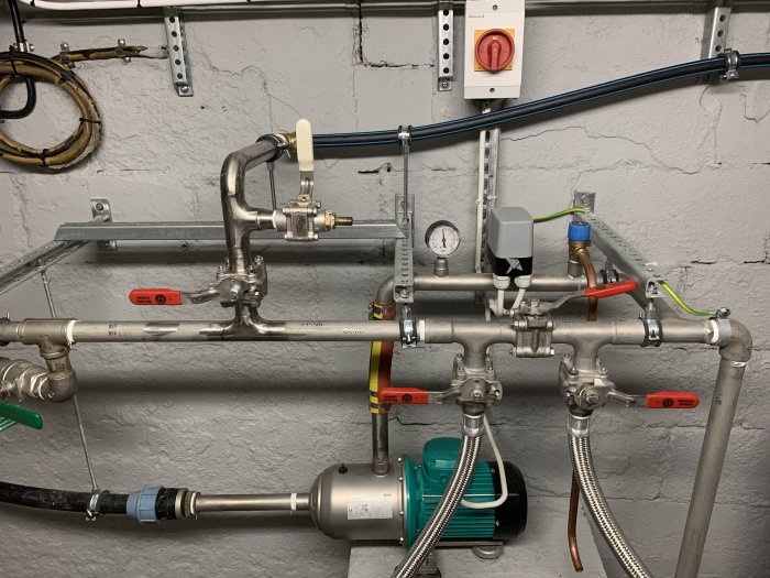Komplex rörsysteminstallation med vattenmeter, ventiler och pump i en källare.