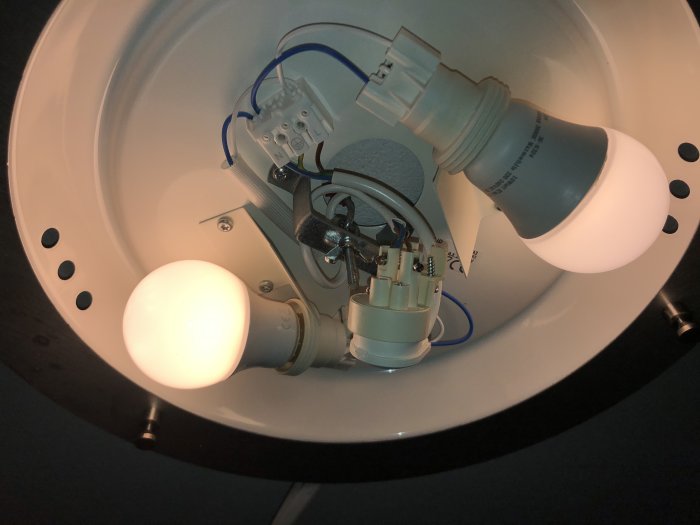 Insidan av en enkel taklampa med tänd glödlampa och synlig elinstallation.