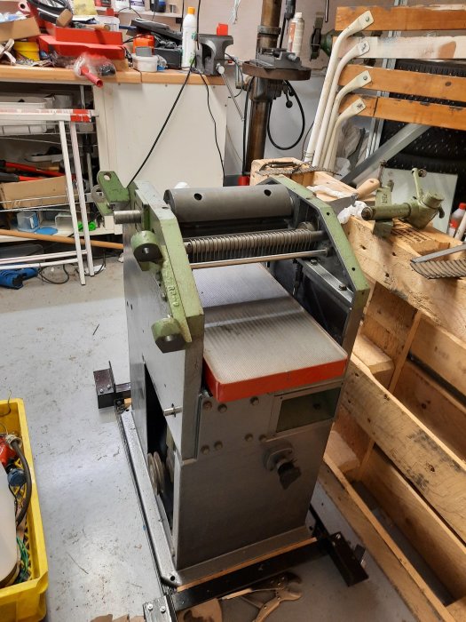 En slipmaskin för slipning av golv står i en verkstad fylld med olika verktyg och byggmaterial.