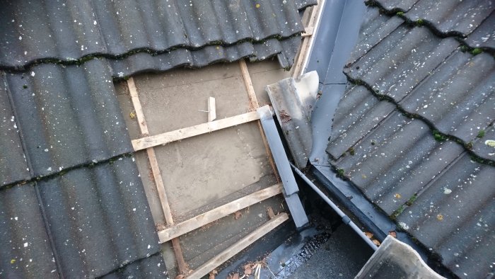Delvis avtäckt tak med underlagspapp och synlig råspont samt angränsande tak med plåt och betongpannor.