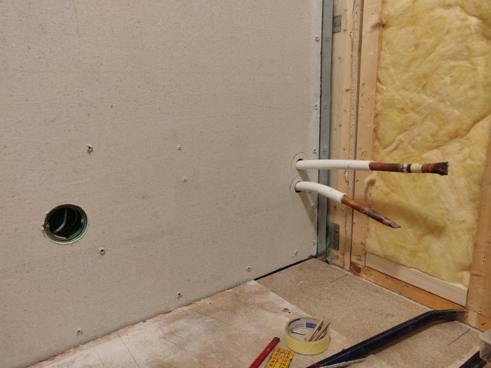 Väggskiva med urtag för tapprör och dosa, värmerör vid taket, och montagedetaljer synliga.