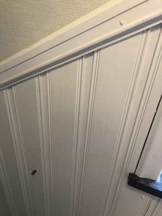 Vit panel i trappa från 70-talet med lodräta brädor och listverk.