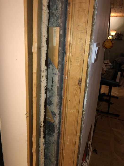 Öppnad vägg med synliga rör och eventuellt asbestisolering mellan murbruket, i ett äldre hus.