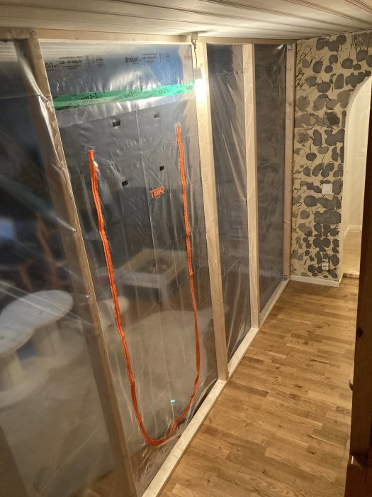 Väggar och dörröppningar skyddade med plast under renovering med synligt rivet innertak.