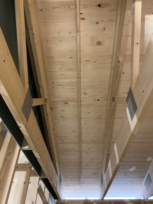 Inre takstruktur i ett garage med påbörjad luftspalt mellan träbalkar och nylagd träpanel.