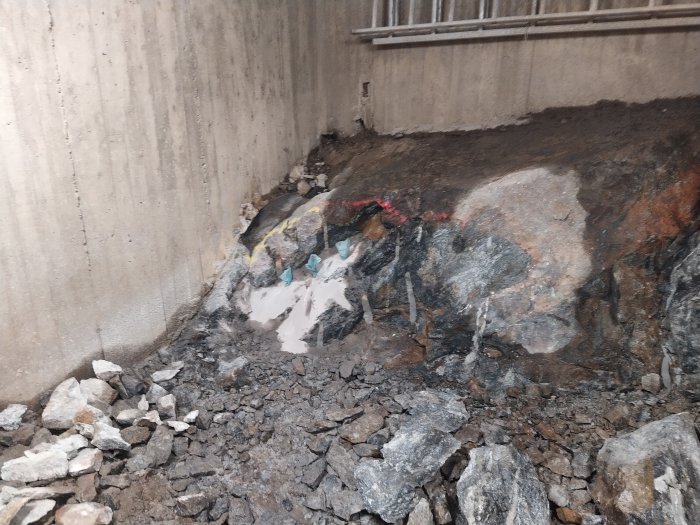 Delvis sprängd bergvägg med lösa stenar och borrningshål efter användning av snigeldynamit och bilhammare.