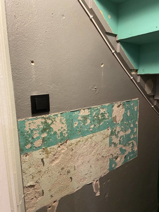 Vägg under renovering med rester av borttaget kakel och exponerad puts.