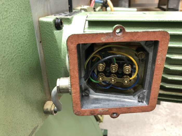 Öppen anslutningslåda på grön maskin med synliga ledningar och elektriska komponenter.