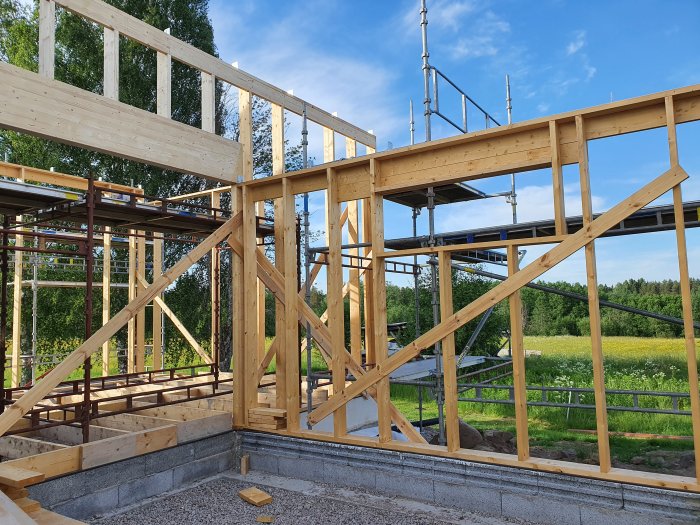 Byggnadsställning och träkonstruktion på husbygge med synlig limträbalk och blå himmel i bakgrunden.