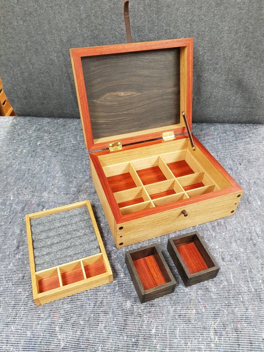 Handgjort smyckeskrin i ek, svartek och paduk med detaljer i mässing och läder, öppet med fack.