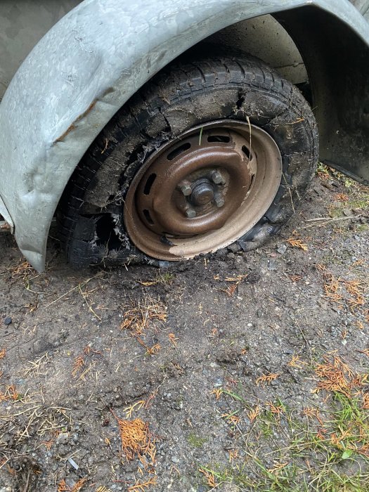 Punkterat släpvagnshjul med synligt trasigt däck och böjd fälg på grusmark.