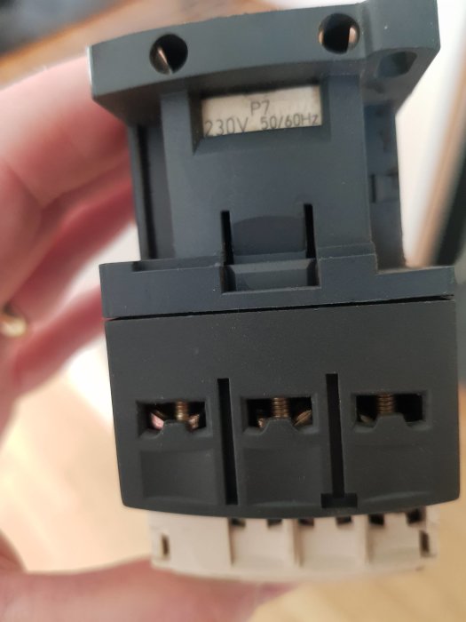 Hand håller ett elektriskt komponent med en etikett som lyder "230V 50/60Hz".
