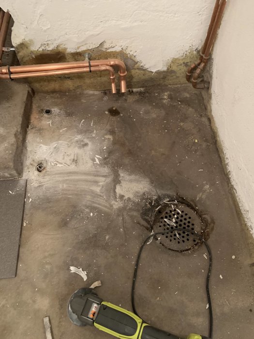 Ojämnt pannrumsgolv med klet, kapade rör och en golvbrunn, renoveringsarbete pågår.