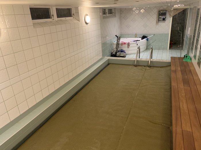 Inomhuspoolrum med kaklade väggar, pooltäckning på poolen, synliga ventilationsöppningar och en luftavfuktare.